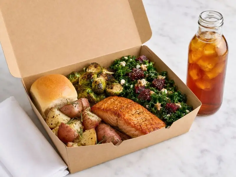 San Jose Catering Company ready-to-serve boxed lunch with seasoned fish, roasted sides, leafy greens, a dinner roll, and beverage.