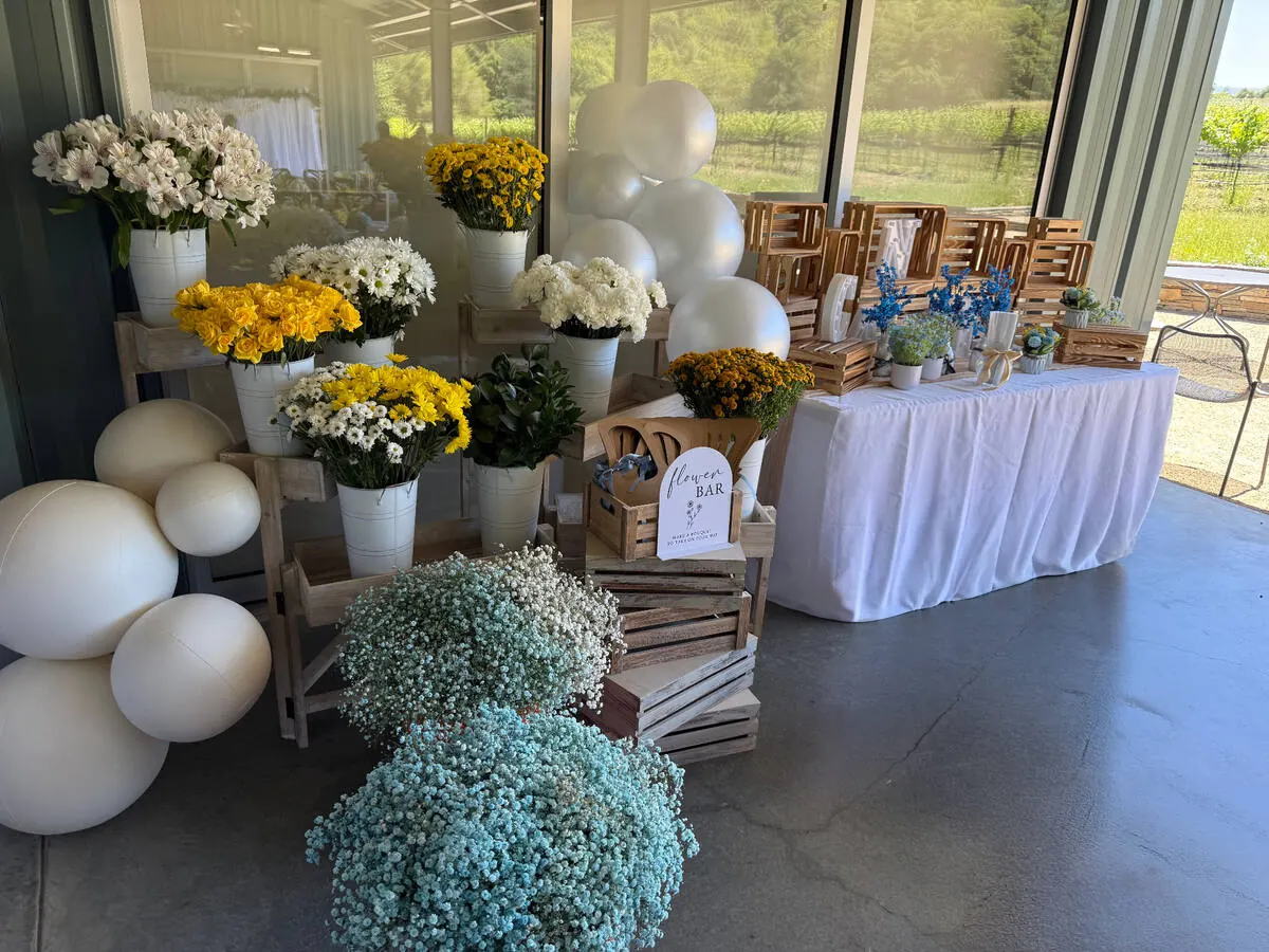 Bloom bar stocked with yellow roses, daisies and baby's breath beside wrapping paper and ribbon for guests to build bouquets — signature bloom bar from Santa Clara catering